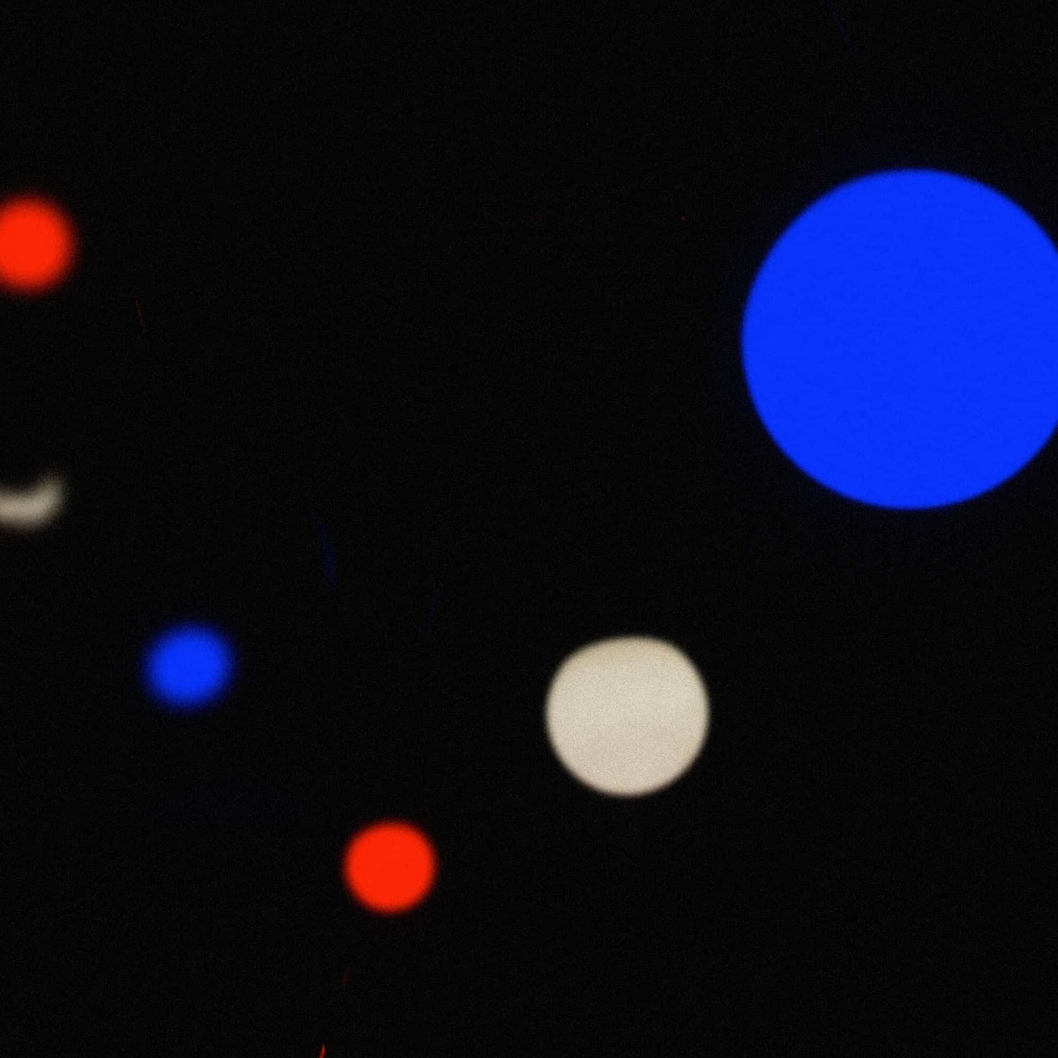 Guirlande lumineuse tricolore floue en situation nocturne, avec des points lumineux bleu, blanc et rouge ressortant sur un fond sombre pour une ambiance festive.