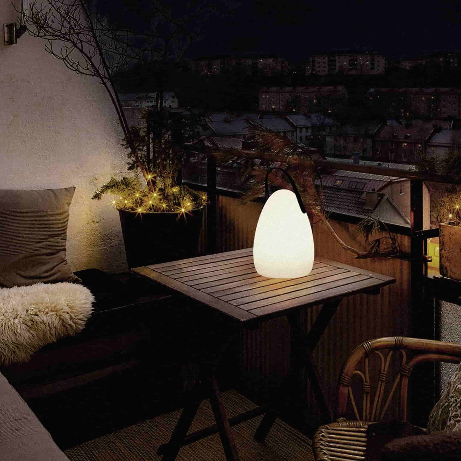 Lampe solaire d’extérieur en forme d’œuf, allumée sur une table en bois sur une terrasse de nuit, diffusant une lumière chaude dans une ambiance cosy.